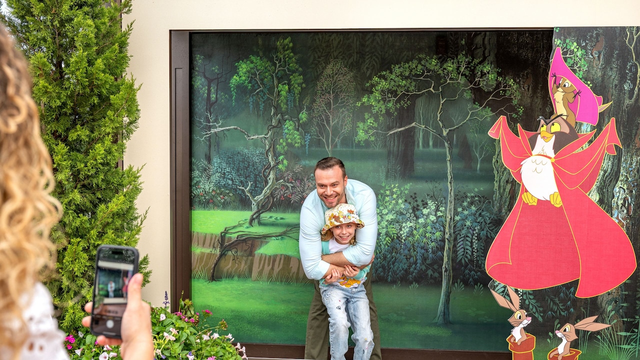 A father and daughter posing in a step in frame with 4 animated forest animals from Sleeping Beauty