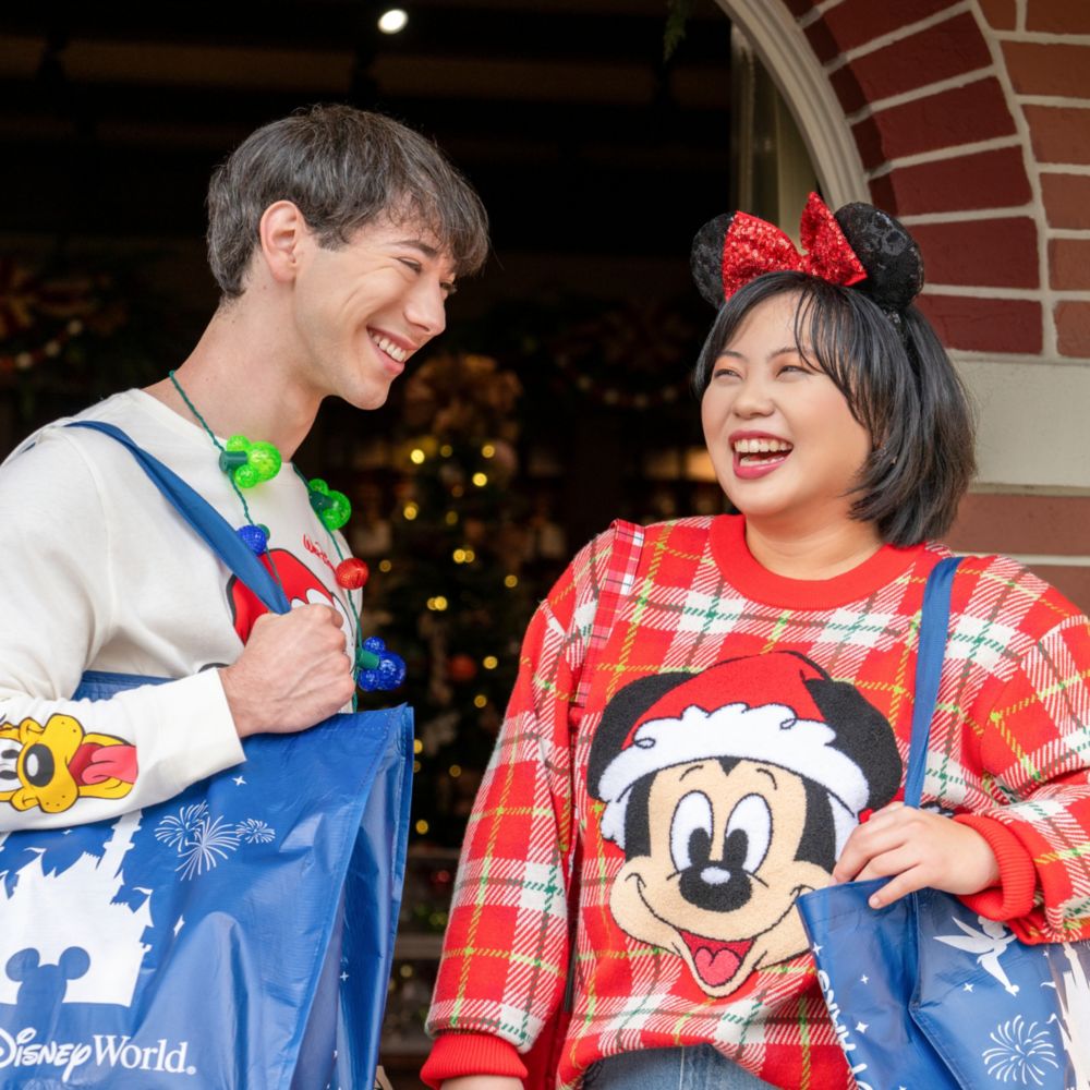 Two Guests wearing Christmas apparel including a sweater featuring Mickey Mouse, a long sleeve shirt featuring Donald Duck, Pluto and Goofy, a Minnie Mouse ear headband and a string light necklace