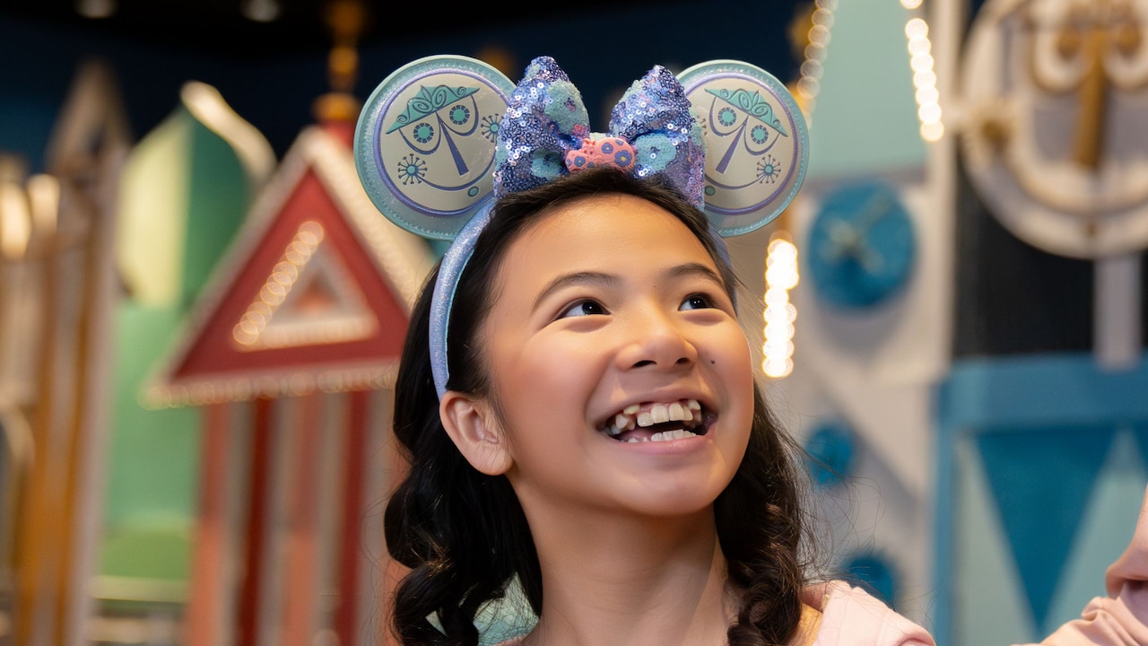 A father beside his daughter wearing an ‘it’s a small world’ Minnie Mouse ear headband inside ‘it’s a small world’