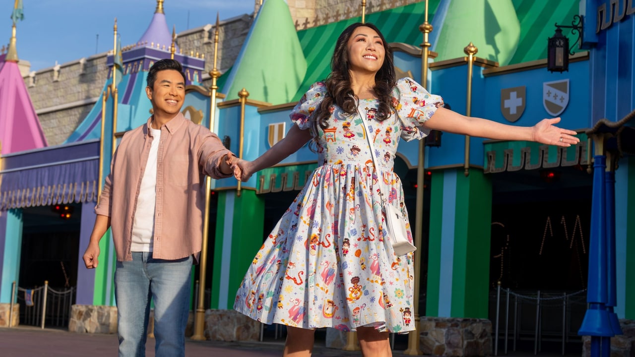 A woman in an ‘it’s a small world’ dress, holding her partner’s hand in front of ‘it’s a small world’