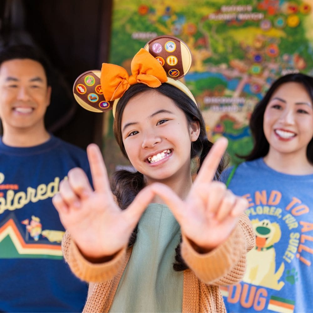 A family of 3 wearing Up themed apparel, including a sweatshirt, T shirt and a Minnie Mouse ear headband