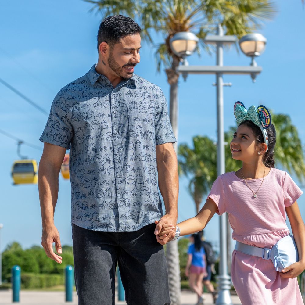 A father wearing a Walt Disney World Resort button up short sleeved shirt and holding hands with his daughter who is wearing a Minnie Mouse ear headband