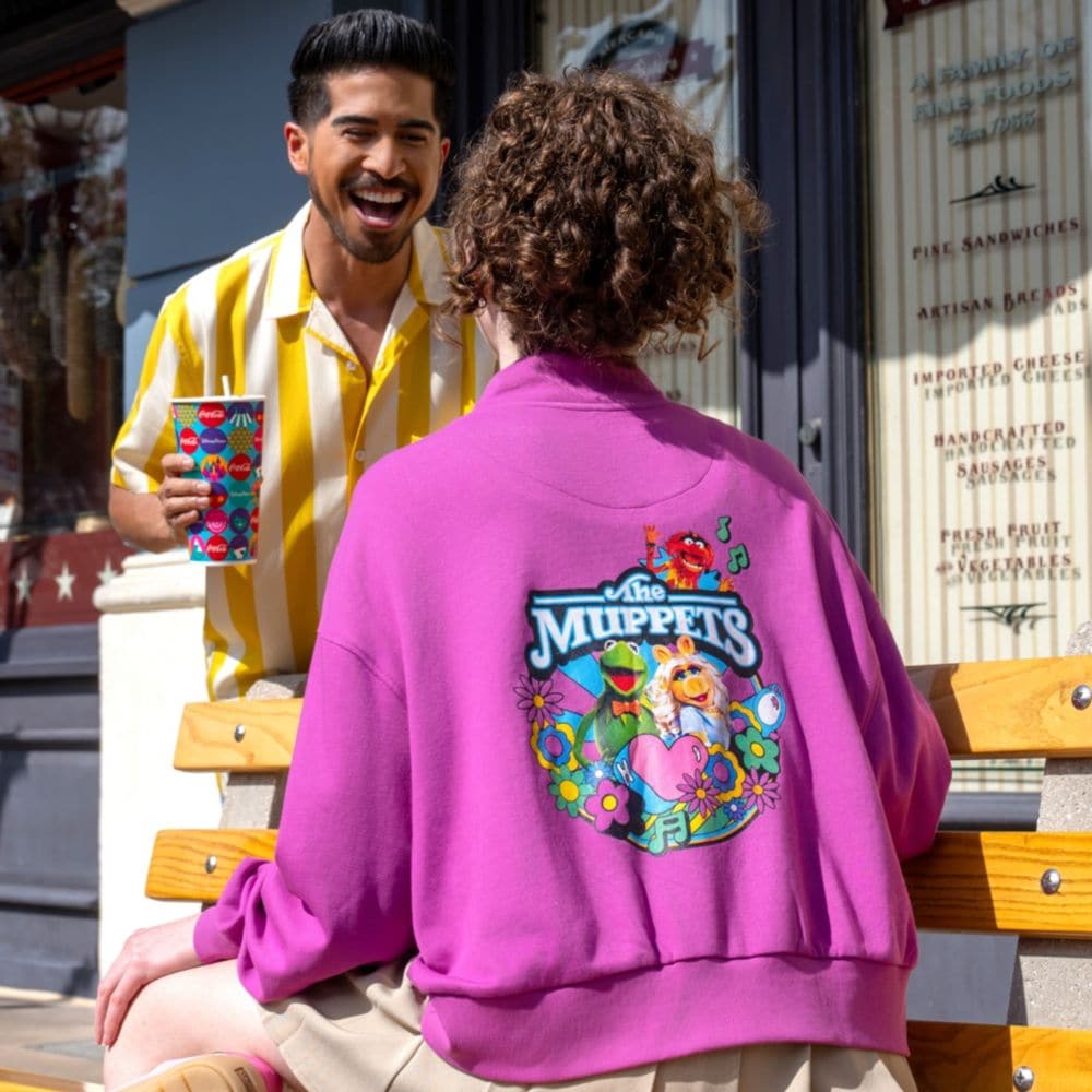 Two Guests conversing while one sits on a bench wearing a Muppets jacket