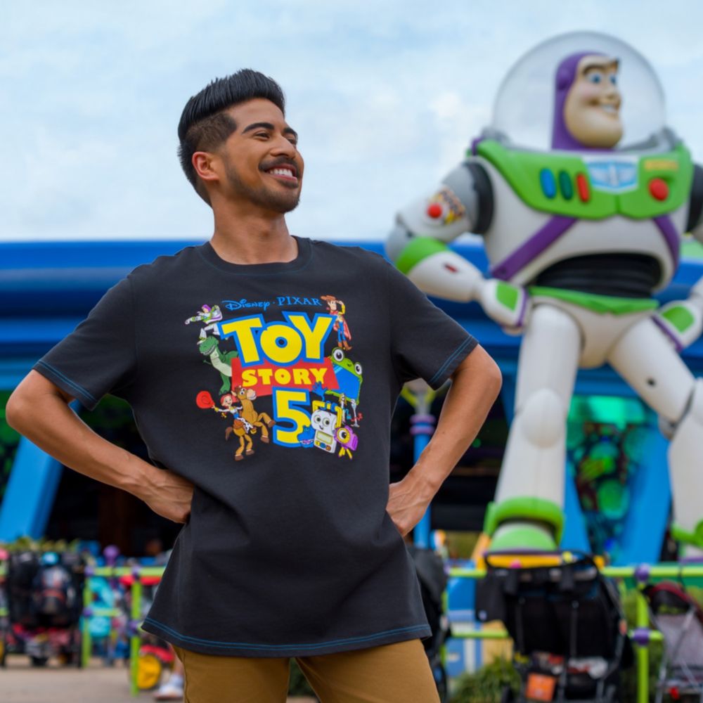 A Guest in a Toy Story shirt posing like the Buzz Lightyear statue near Alien Swirling Saucers at Disney's Hollywood Studios theme park