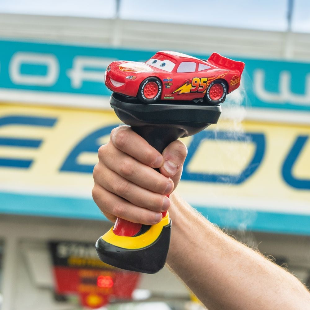 A hand raising a Lightning McQueen light up wand, with the Tomorrowland Speedway sign in the background
