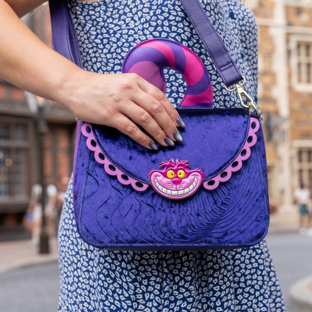 A woman carrying a velvet handbag featuring a Cheshire Cat face and a striped tail shaped handle