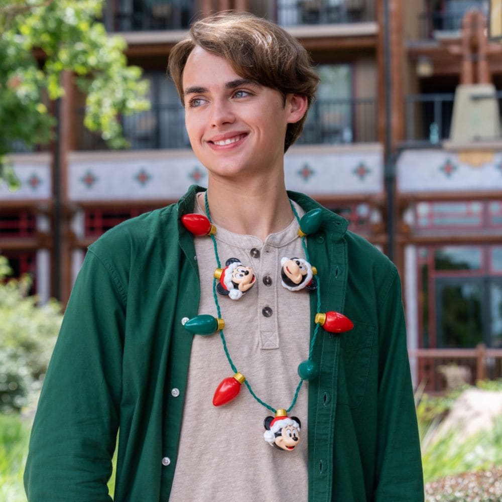 A man wearing a holiday light necklace featuring Mickey Mouse ornaments