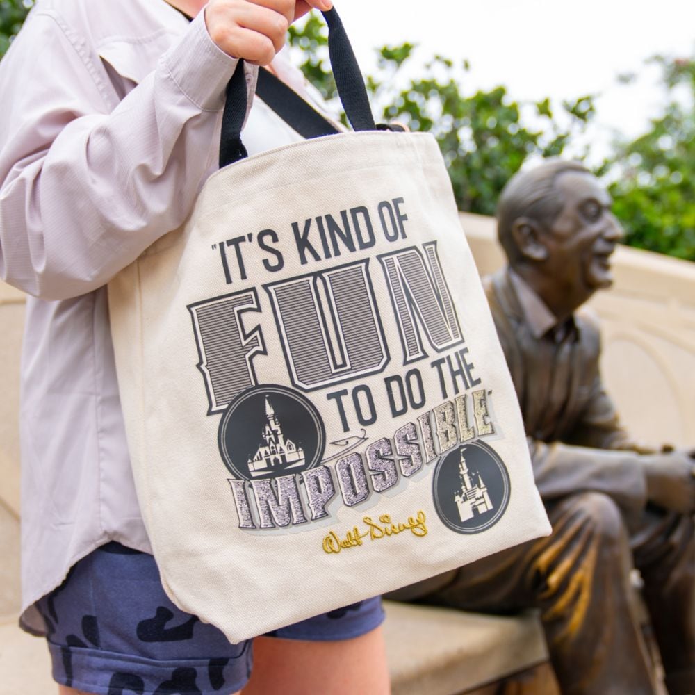 A person carrying a canvas tote bag printed with the quote ‘It's kind of fun to do the impossible’ attributed to Walt Disney