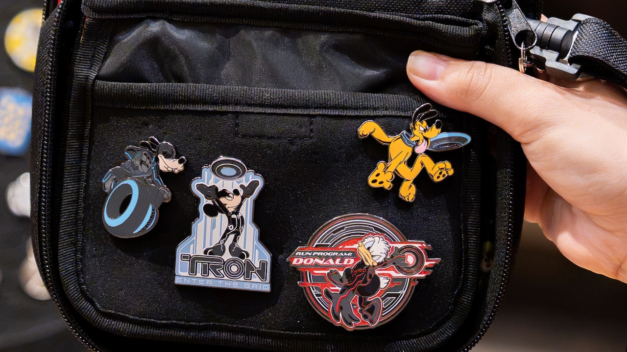 A hand holding a bag of Disney holiday pins, with a Mickey-shaped pin trading board in the background