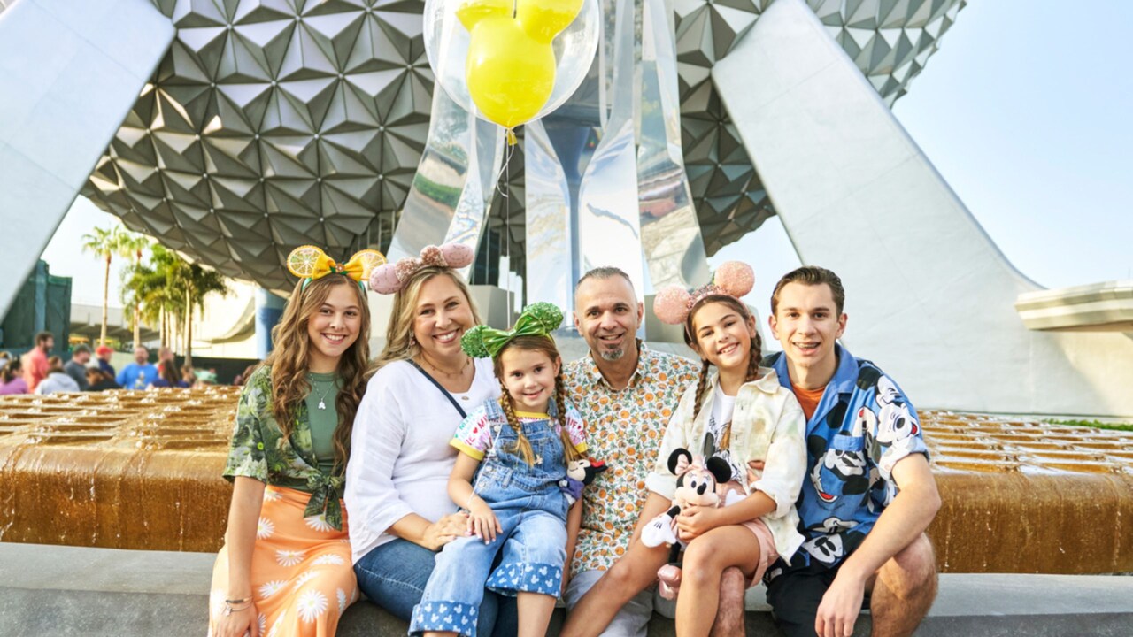 A family smiling and sitting on the edge of the fountain in front of Spaceship Earth at Epcot