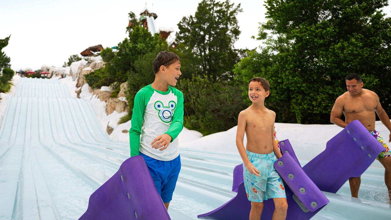 A family carrying mats as they walk out of the Toboggan Racers waterslide at Disney's Blizzard Beach water park