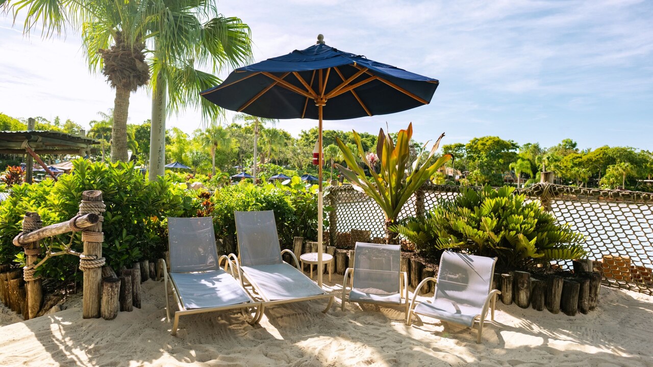 Beach loungers and chairs under an umbrella in a sandy area at Disney’s Typhoon Lagoon water park