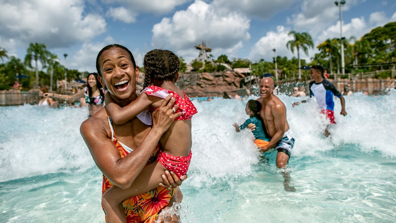 A Guest carrying a child while walking out of the Typhoon Lagoon Surf Pool at Disney’s Typhoon Lagoon water park