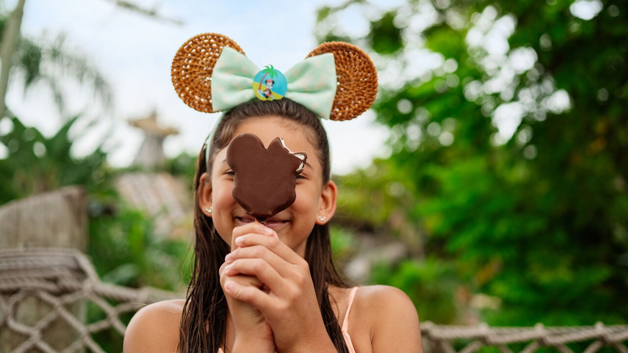 A girl smiling while holding a Mickey Mouse ice cream bar in front of her face