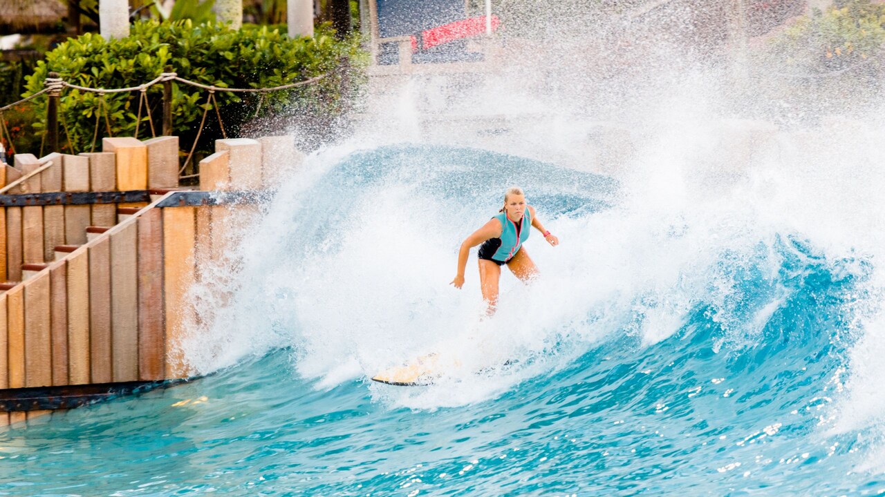 A woman in a life preserver surfing in a wave pool