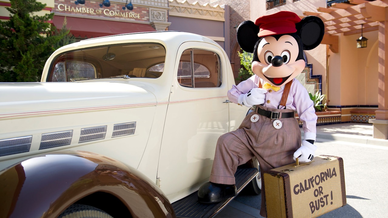 Mickey Mouse in a director’s outfit posing next to a classic car at Disney’s California Adventure Park