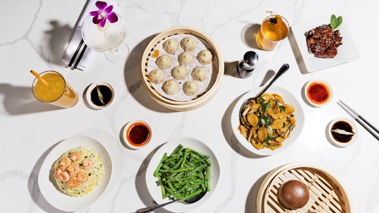 Table set with Asian inspired foods like dumplings, green beans and shrimp fried rice, with beverages, chopsticks and sauces