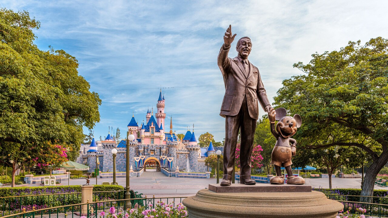 A bronze statue of Walt Disney holding hands with Mickey Mouse in front of Sleeping Beauty Castle