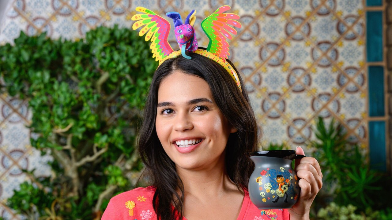 A girl modeling Coco themed gear and a Dante alebrije headband, and holding a Miguel coffee mug