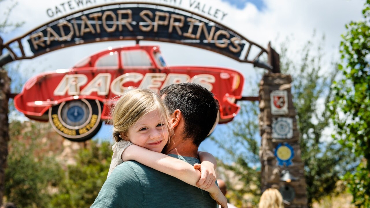Un padre abrazando a su hijo frente a la marquesina de Radiator Springs Racers