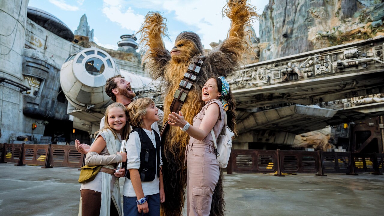 A family of 4 posing for a photo with Chewbacca at Star Wars Galaxy’s Edge in Disney’s Hollywood Studios