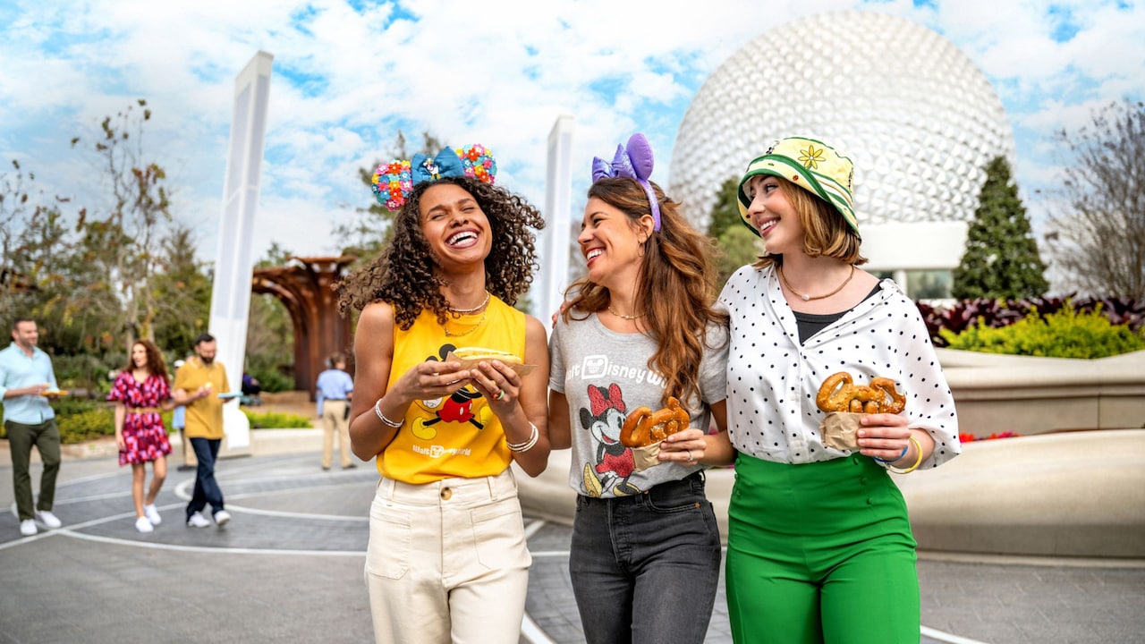 3 women share a friendly laugh as one eats a hot dog and the other 2 enjoy Mickey shaped pretzels