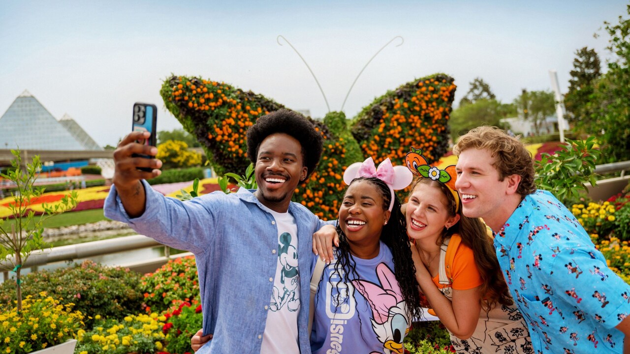 2 couples pose together for a selfie in front of a giant butterfly topiary