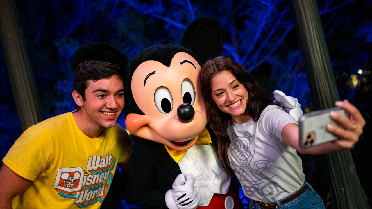 A couple smiles for a selfie with Mickey Mouse