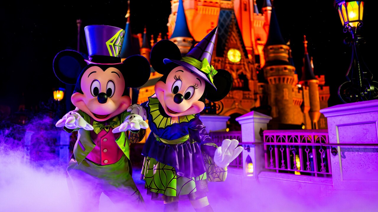 Mickey Mouse and Minnie Mouse, in spooky Halloween costumes, stand in a fog surrounding Cinderella Castle
