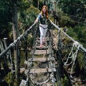 A woman with a harness smiles as she crosss a rope bridge