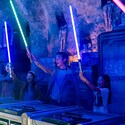 Five Guests standing around a circular table holding up their custom, hand-built lightsabers at Savi's Workshop in Disney's Hollywood Studios in Florida