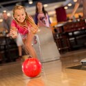 A smiling young girl bowls with both hands while her family watches in the background at Splitsville Luxury Lanes in Downtown Disney Area