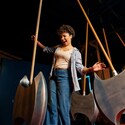 A young woman laughing while navigating between large swinging axe like pendulums in a darkened challenge room