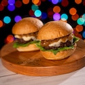 Holiday snacking reaches new heights with these irresistible sliders at Disney Jollywood Nights. Two beef sliders topped with melted cheese, caramelized onions and leafy greens on a wooden serving board
