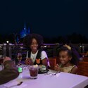 A young family of 4 dining together with Cinderella Castle glowing in the distance