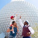 A young boy sitting on his father’s shoulders, giving a high five to a VIP Tour Guide in EPCOT