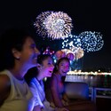 Three girls wearing Minnie Mouse ear headbands enjoying a nighttime fireworks display on a boat