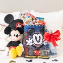 A Mickey Mouse plushie, ear hat and drawstring bag on a hotel bed next to a Disney bottle, lanyard, notepads and pens