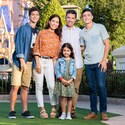 A family with 2 teen boys and a young girl are all smiles as they stand in front of Cinderella Castle