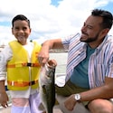 A smiling father and a son proudly hold up a large fish on a boat