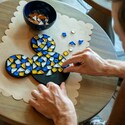 A man gluing stones onto a Mickey Mouse shaped object to create a mosaic art piece 