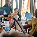 A woman holds up her painting of Cinderella Castle surrounded by fireworks during a painting class 