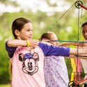 A Cast Member demonstrating proper form to 2 young girls pulling arrows back on bows
