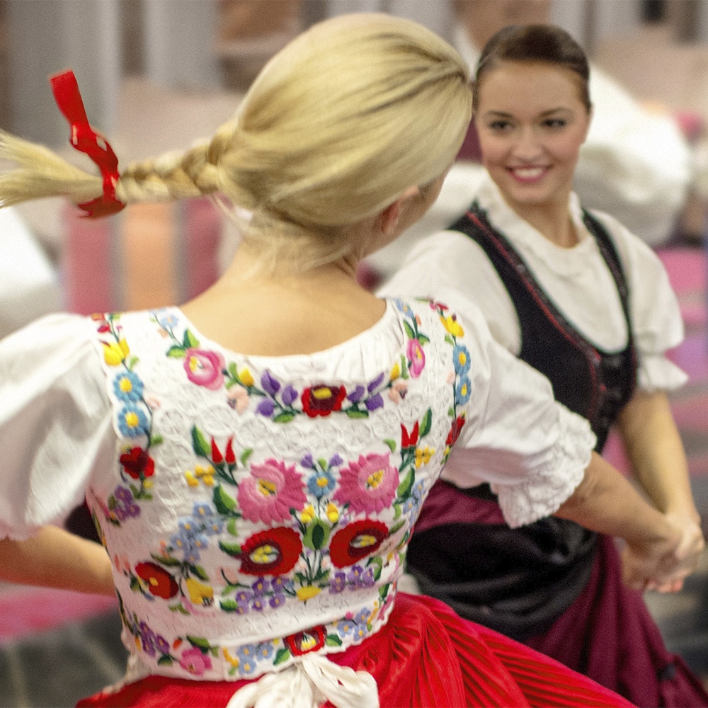 2 German women and a man dance a folkdance wearing traditional embroidered costumes 2 German women and a man dance a folkdance wearing traditional embroidered costumes