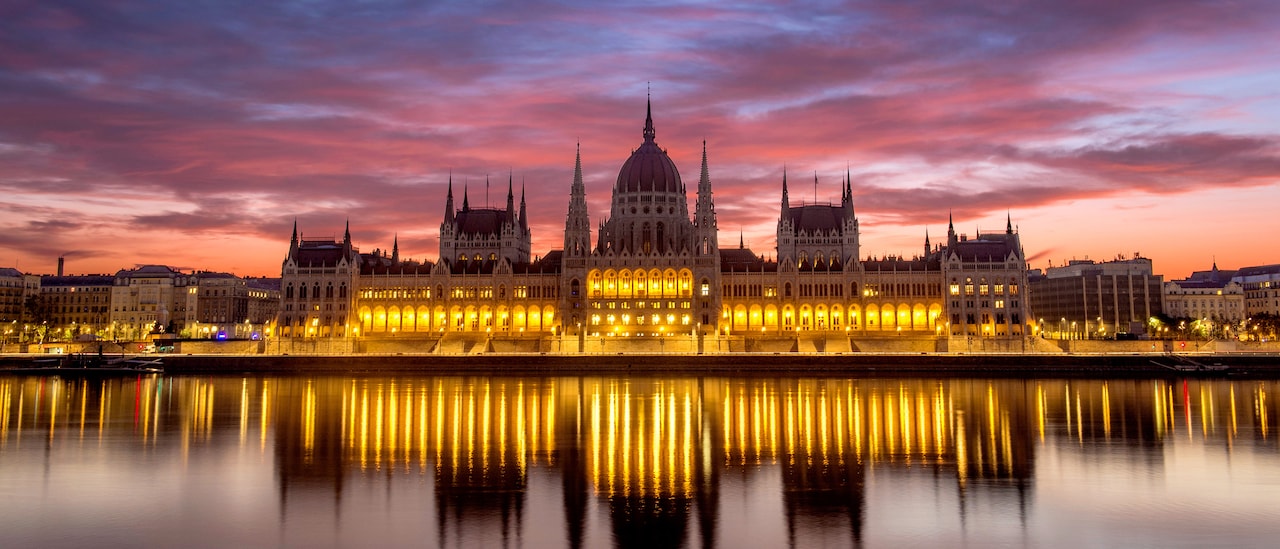 The Budapest Parliament building at sunset, with reflections of its lights on the Danube River The Budapest Parliament building at sunset, with reflections of its lights on the Danube River