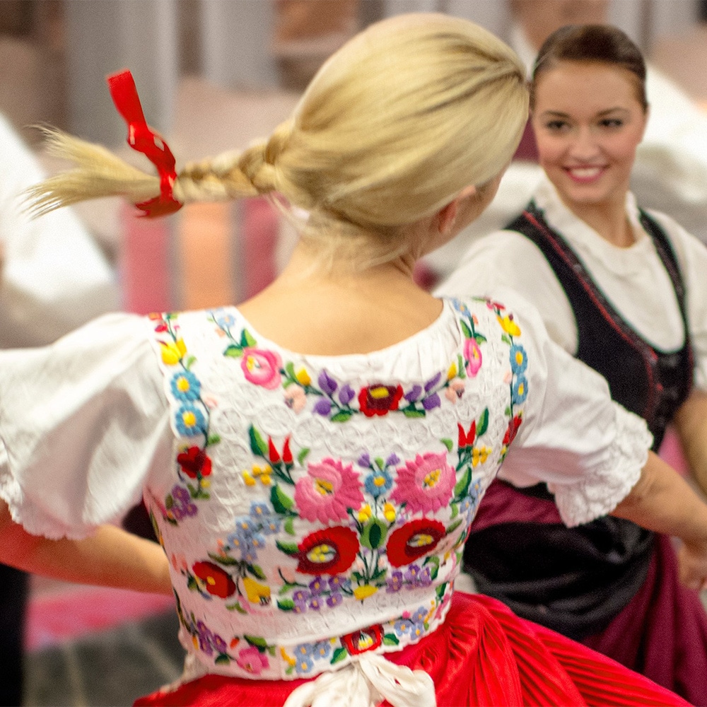 2 women wearing traditional costumes dance as a costumed male dancer claps 2 women wearing traditional costumes dance as a costumed male dancer claps