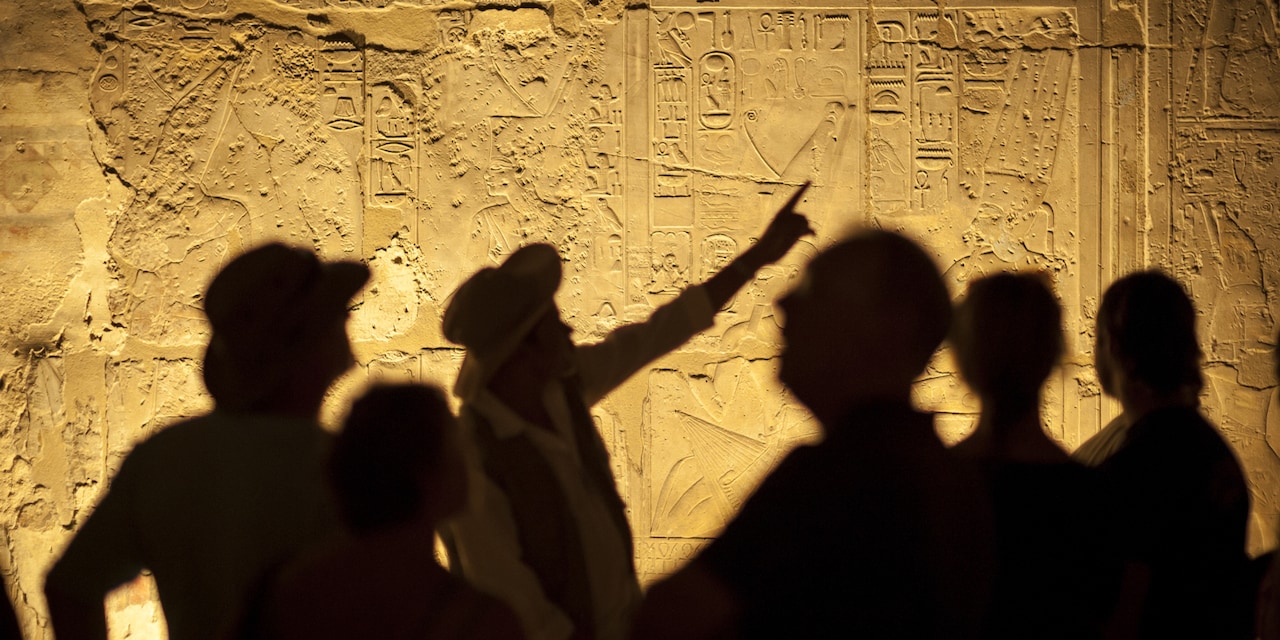 An Egyptologist stands in front of a tour group and points to hieroglyphics An Egyptologist stands in front of a tour group and points to hieroglyphics