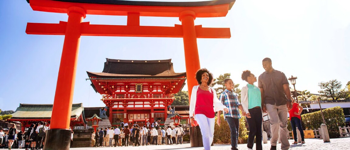 A family of 3 and an Adventure Guide walk in front of the Fushimi Inari Shrine in Kyoto, Japan