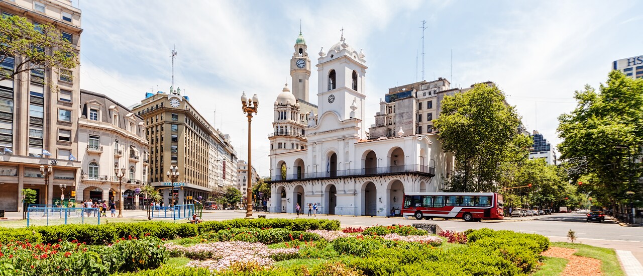 Bus passing in front of a building with a tower that is by a landscaped square