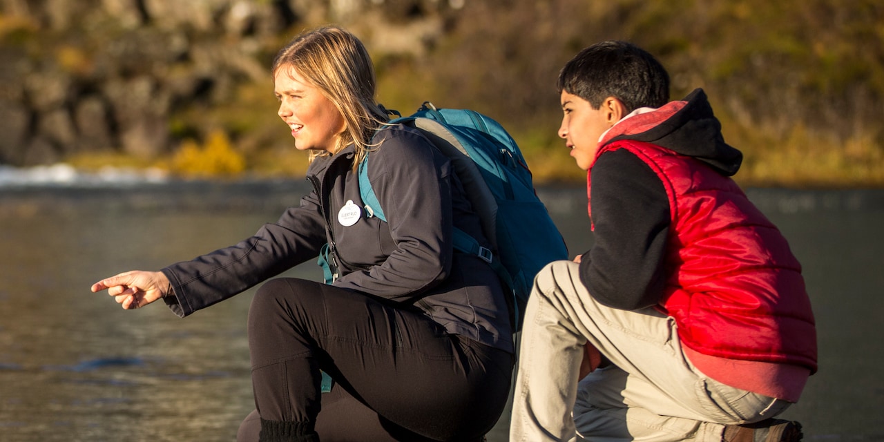 An Adventure Guide and a boy squatting on a rocky surface, looking at a site in the distance An Adventure Guide and a boy squatting on a rocky surface, looking at a site in the distance